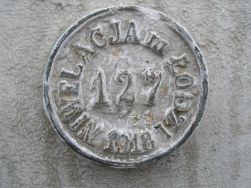 Centralny reper nr 127 ł&oacute;dzkiej sieci niwelacyjnej, osadzony na ścianie narożnej kamienicy przy zbiegu  ulic Tuwima (Przejazd) i Sienkiewicza. Fotografia Zdzisława Szambelana.
